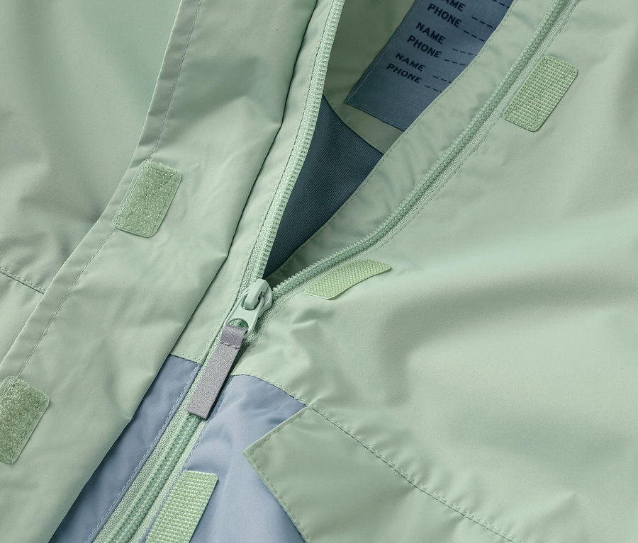 Detailní záběr na rozepnutou mátově zelenou bundu se zipem a světle modrými akcenty.