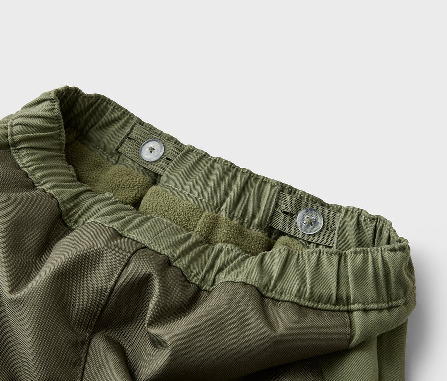 Detailní záběr na olivově zelené kalhoty s nastavitelným pasem a fleecovou podšívkou.