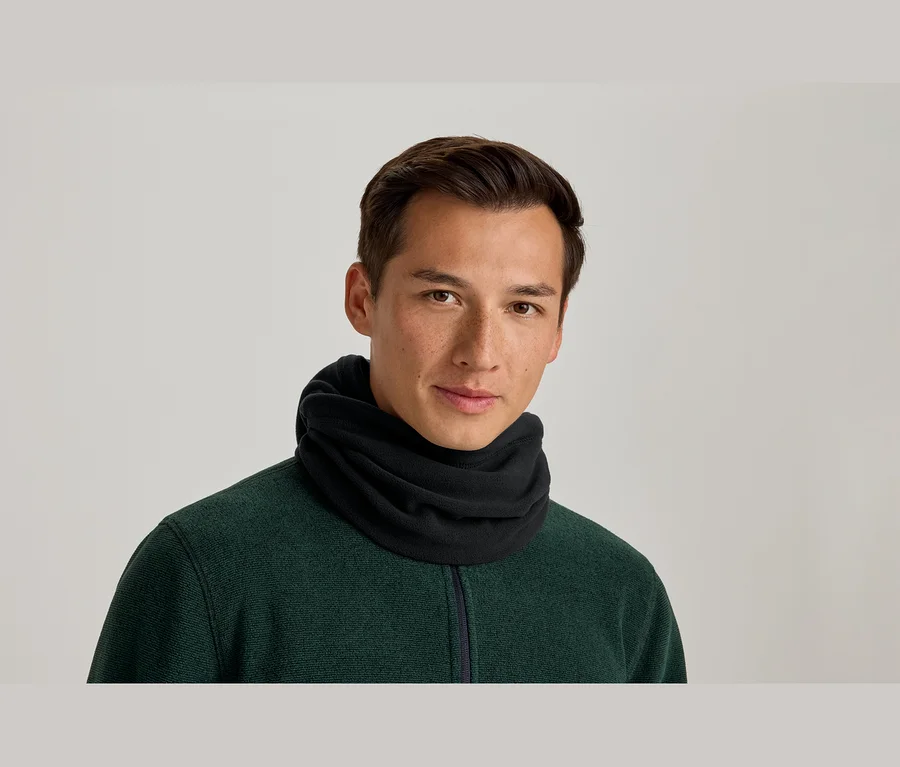 Muž v černém nákrčníku a tmavě zeleném topu na zip, s mírným úsměvem hledí do kamery.