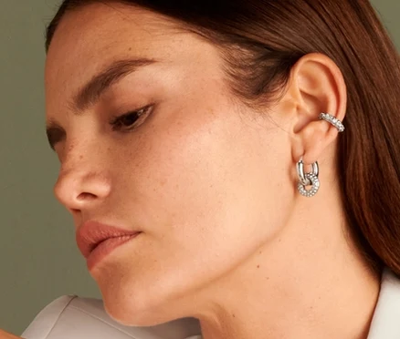 Žena sedí a má na sobě náušnici Ear cuff Sparkle Donut, prsten Sparkle Donut, kreolky Sparkle Donut a řetízek Sparkle Donut.
