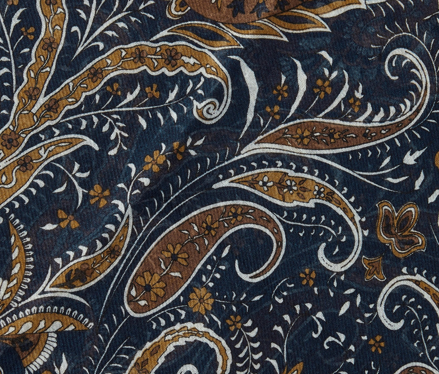 Detailní záběr tkané šály s hnědým a bílým vzorem paisley na tmavě modrém pozadí.