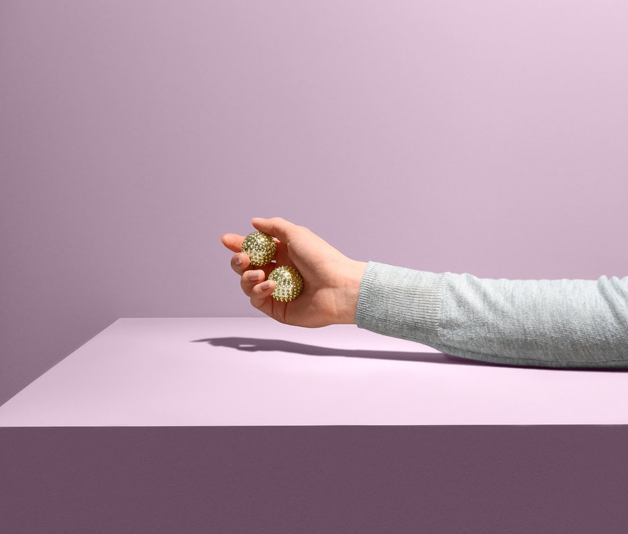 Ruka drží dva Kuličky na prstovou gymnastiku nad fialovým povrchem.