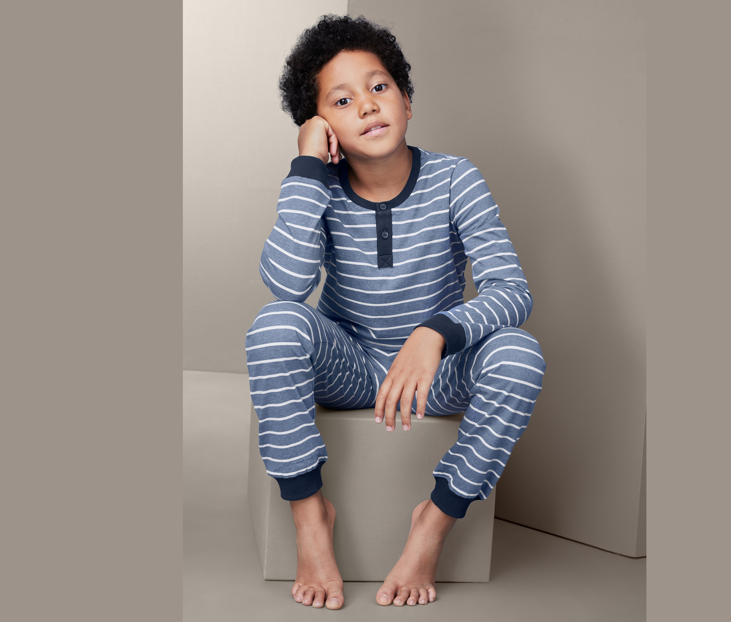 Chlapec sedí a má na sobě dětské pyžamo s modrými a bílými pruhy.