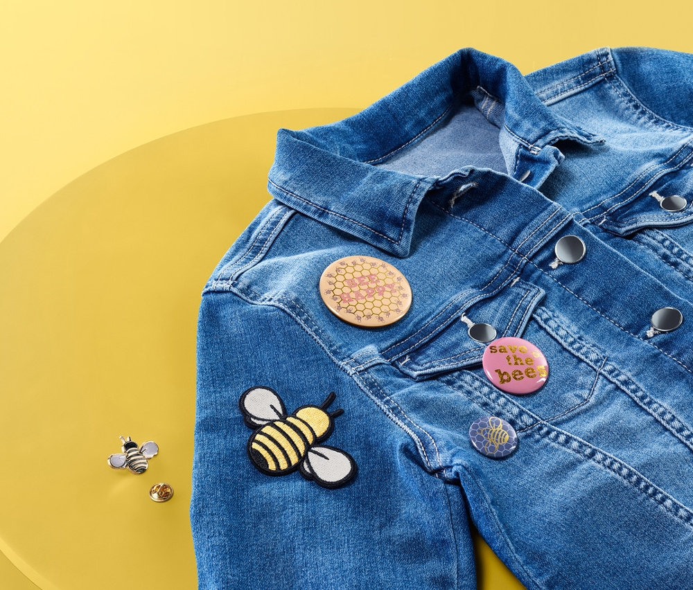 Džínová bunda leží na žlutém stole a má na sobě sadu připínacích a nažehlovacích motivů Včela.