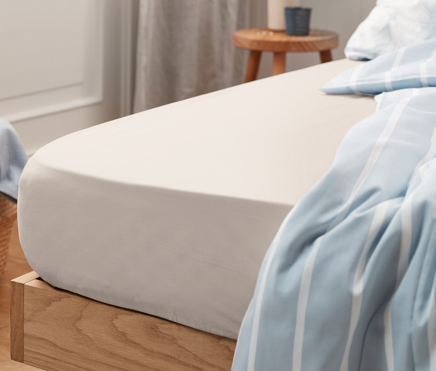 Béžové jersey prostěradlo na posteli s dřevěným rámem a modrobílou pruhovanou dekou.