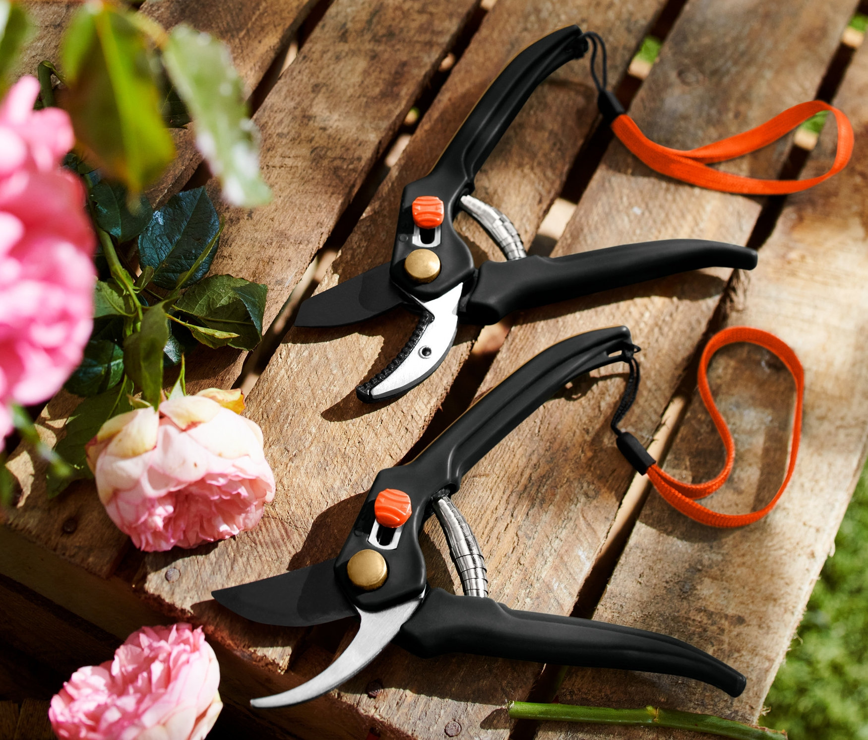 Dvoje zahradní nůžky na dřevěné paletě, vlevo růžové růže.