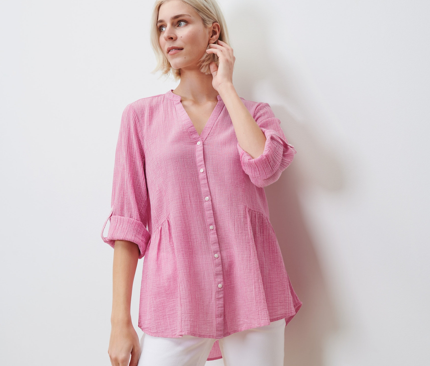 Žena pózuje v pruhované dlouhé tunice a bílých kalhotách.