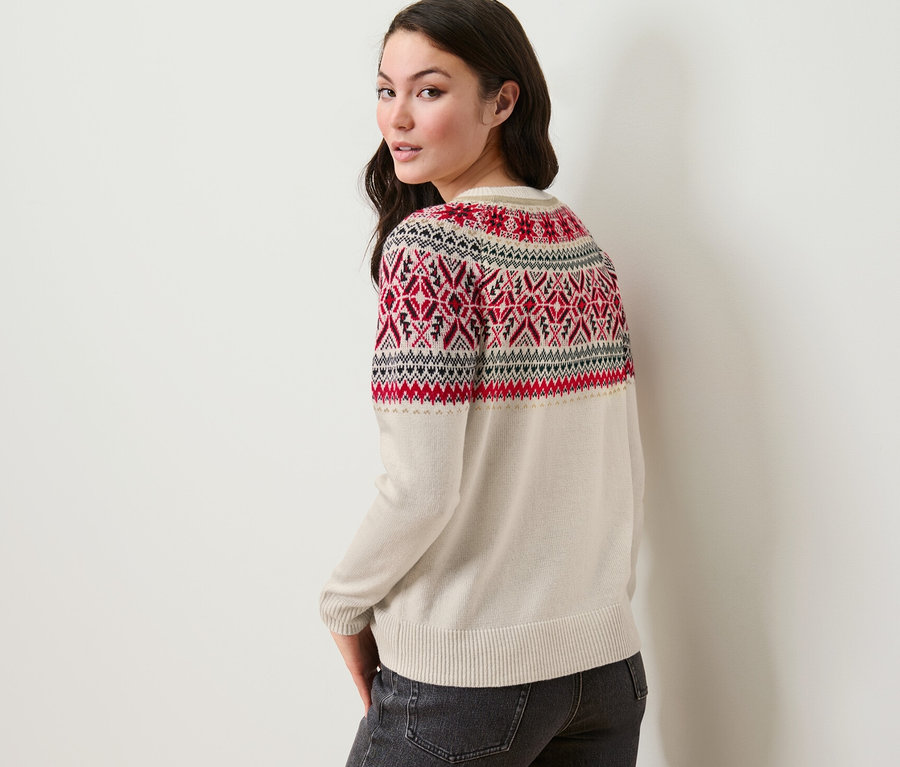 Žena se dívá přes rameno a má na sobě pletený svetr s norským vzorem a džíny.