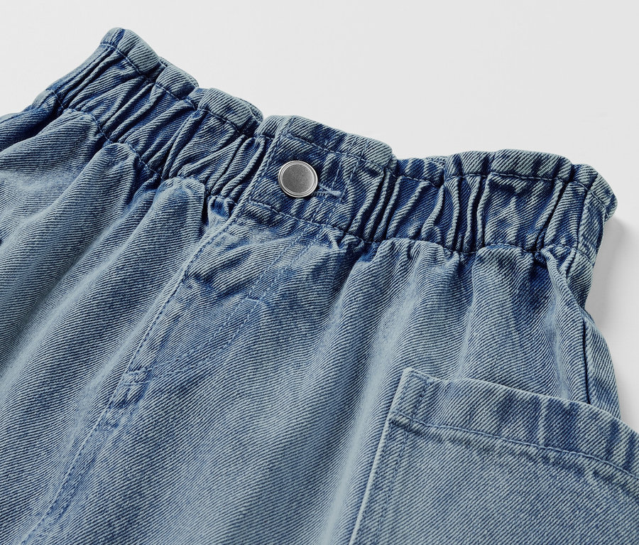 Detail dívčí džínové sukně paperbag se zapínáním na knoflík a kapsami.