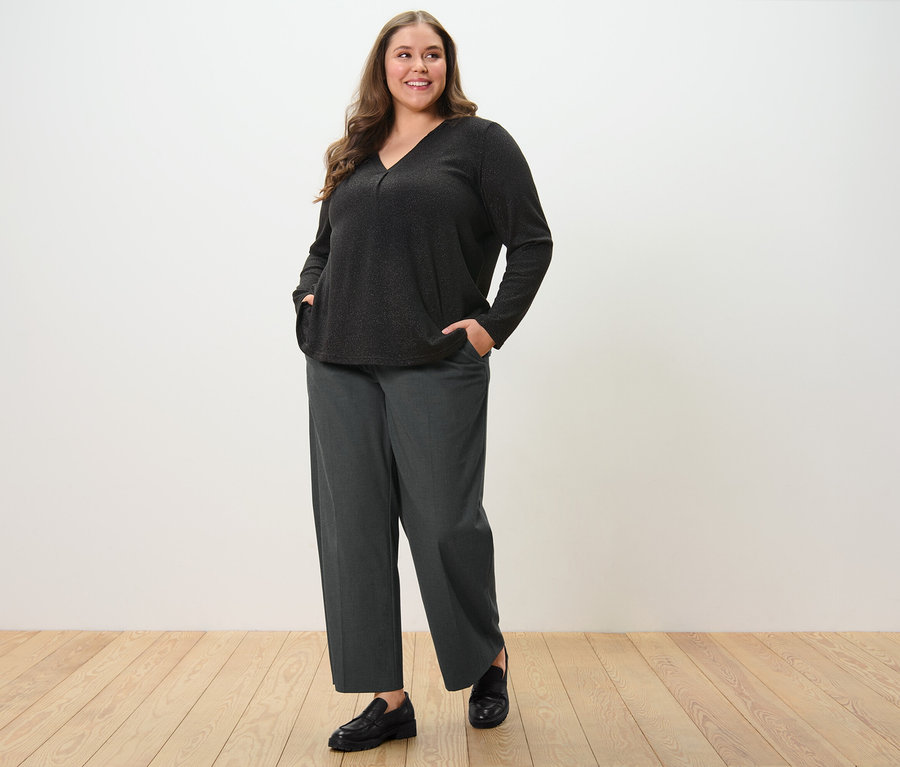 Žena pózuje v pohodlných tkaných kalhotách a halence se třpytivým efektem.