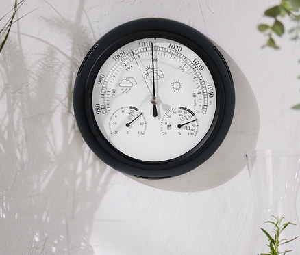 Na zdi visí analogová meteorologická stanice.