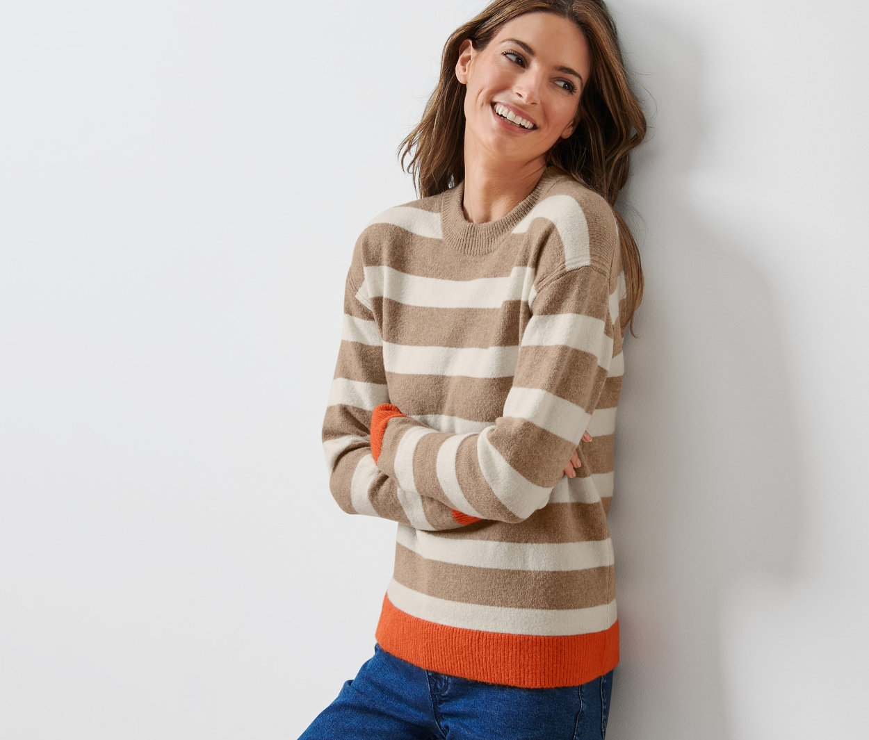 Žena se usmívá a opírá o zeď v pruhovaném pleteném svetru.