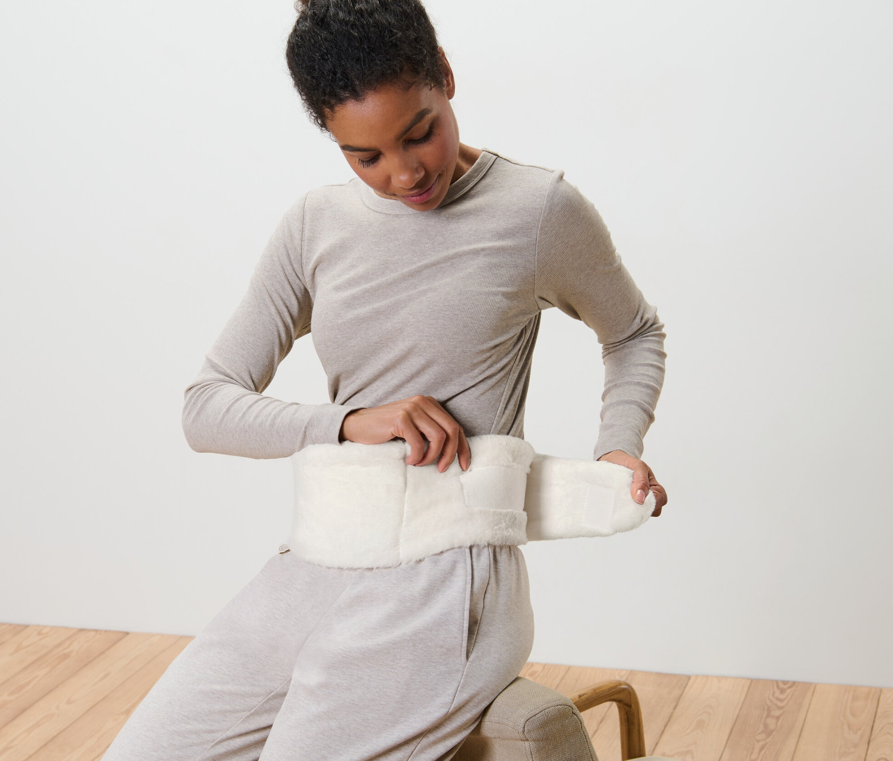 Žena si upevňuje termofor s popruhem kolem pasu.