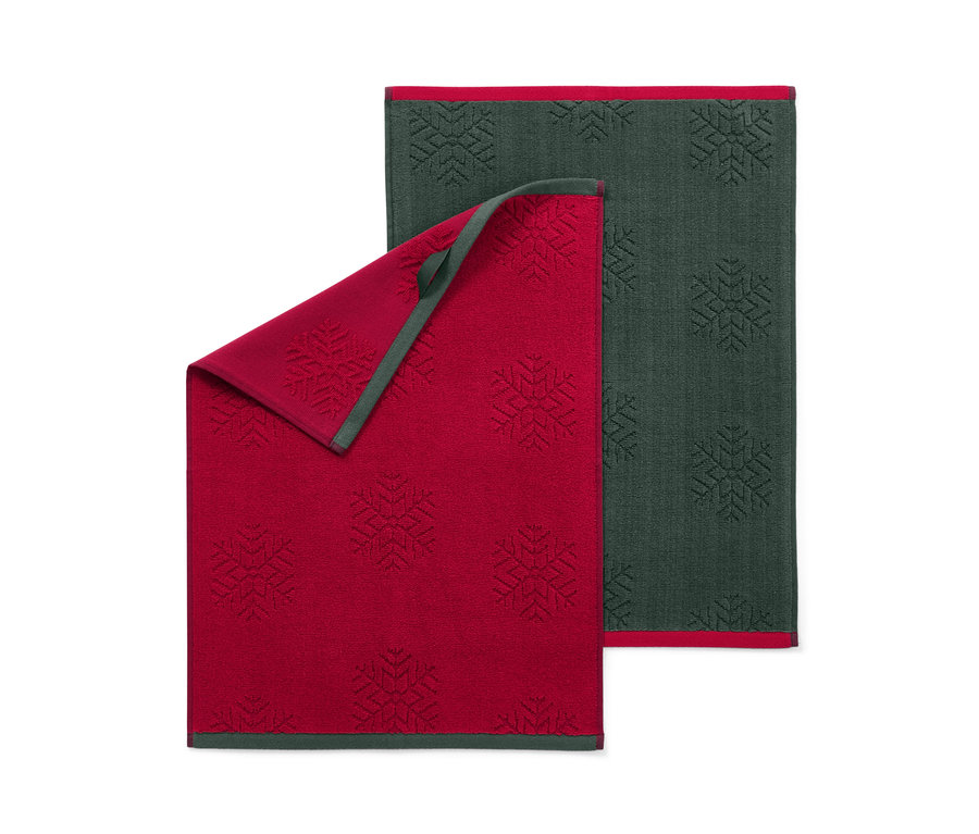 Dva kuchyňské ručníky s motivem sněhových vloček, jeden červený a jeden tmavě zelený.