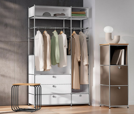 Interiér s bílými dveřmi, kovovou skříní »CN3« se dvěma šatními tyčemi a čtyřmi zásuvkami, úzkou kovovou komodou »CN3« s dřevěnou deskou, hnědošedou, designovou stolní LED lampou a stoličkou.