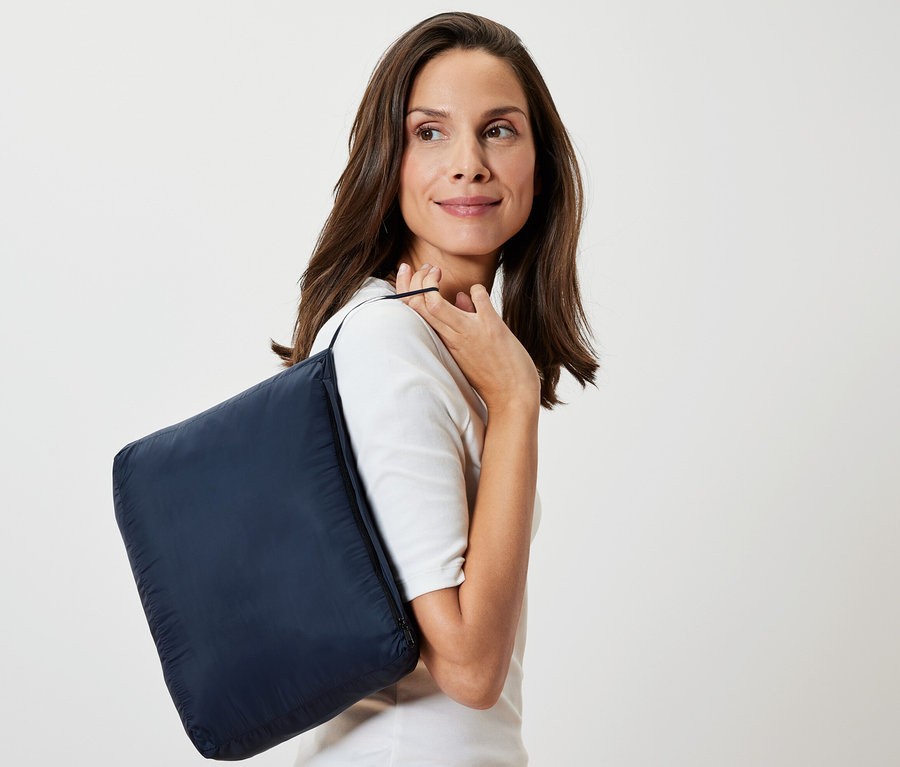 Žena s tmavě modrou cestovní dekou "Velmi lehká cestovní deka" přes rameno.