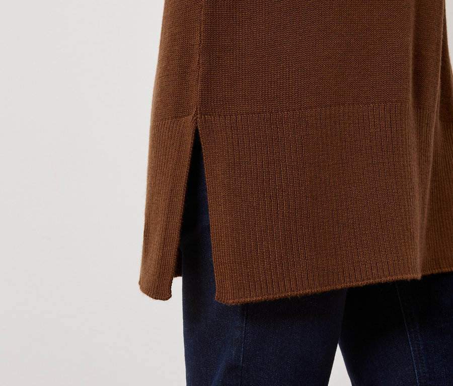 Detail hnědého svetru s rozparkem na boku a tmavě modrých džínů.