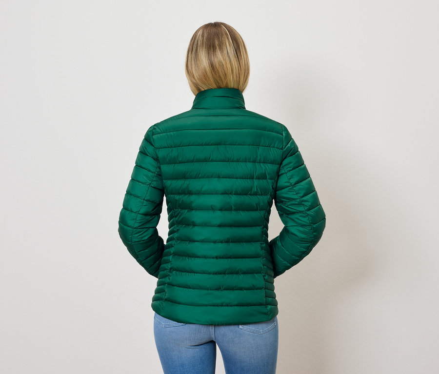 Zezadu pohled na ženu s blond vlasy v zelené prošívané bundě a modrých džínách.