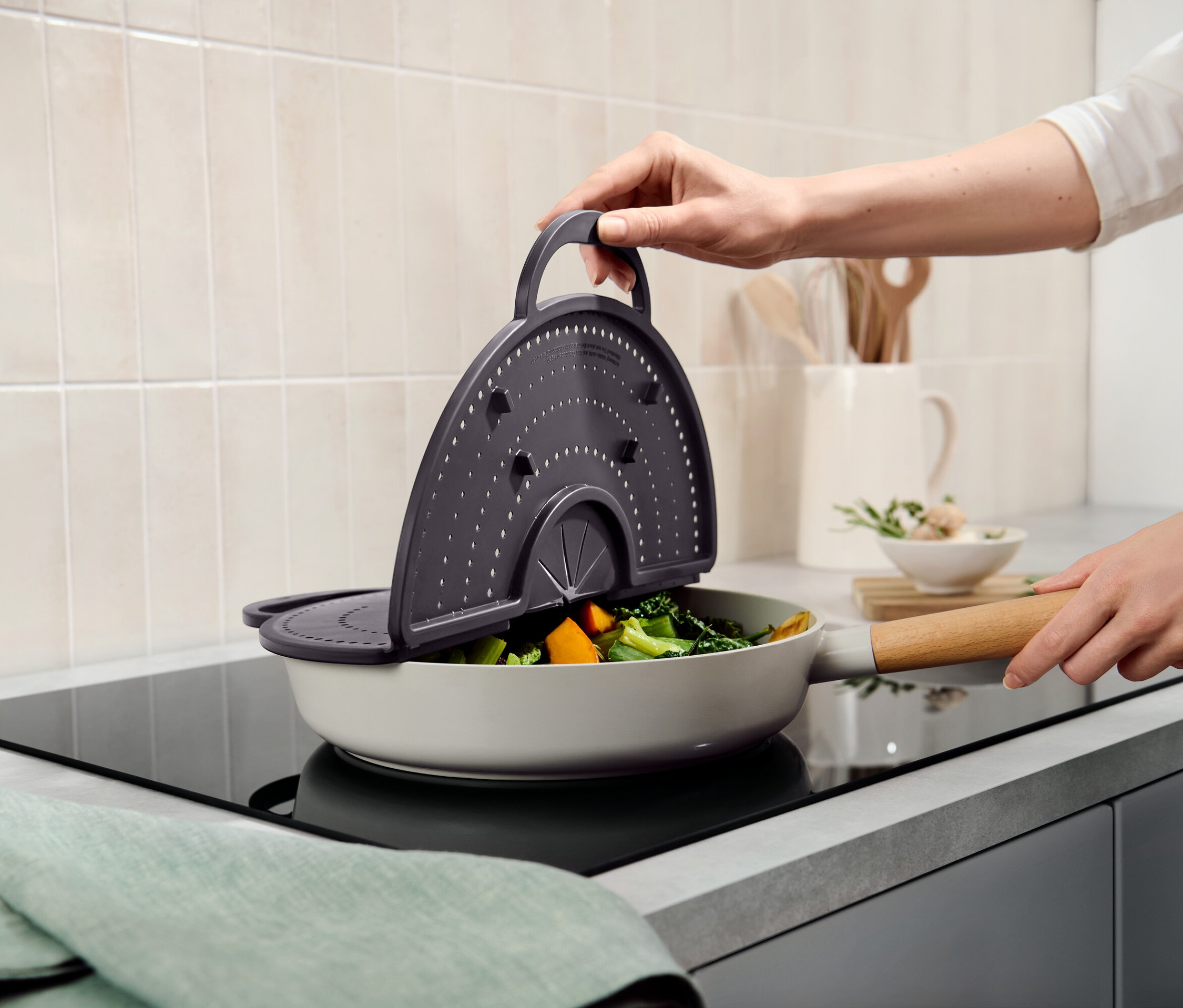 Ruka drží šedé sítko nad pánví se zeleninou.