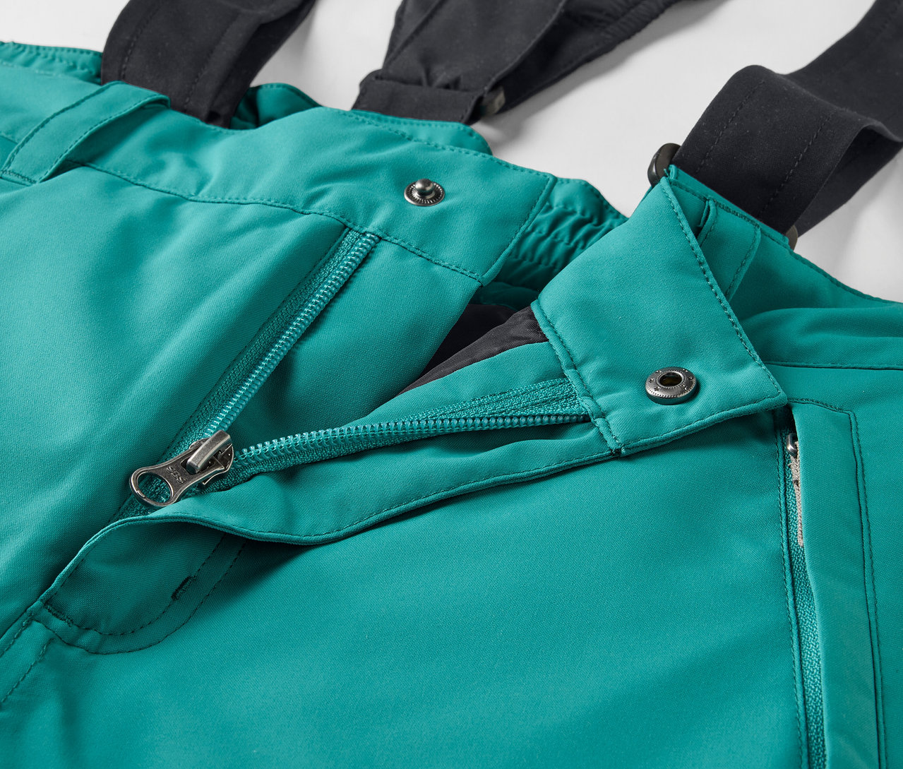 Detail zelených lyžařských kalhot s černými šlemi a rozepnutým zipem.