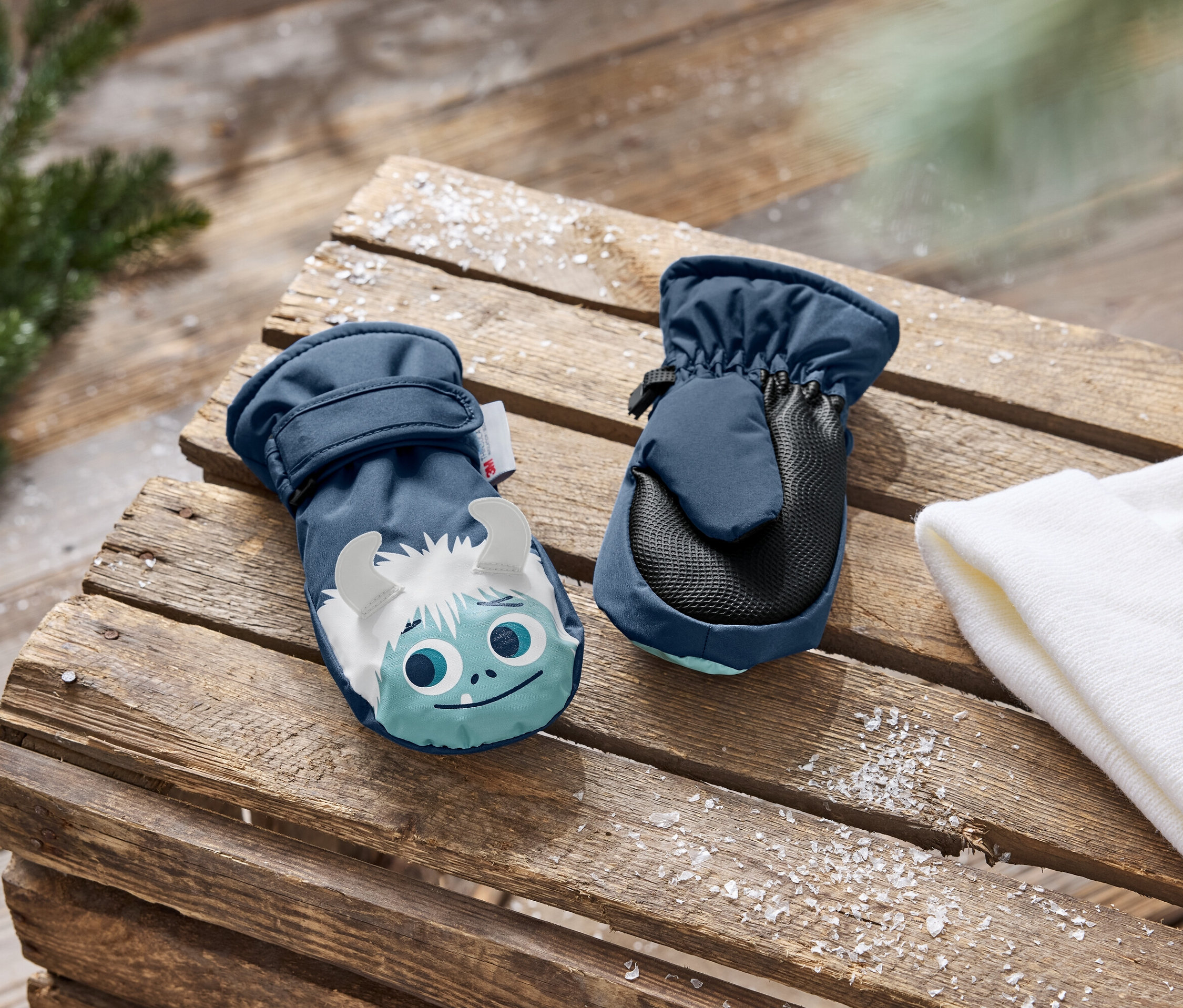 Dvě tmavě modré dětské palčáky s potiskem sněžného muže na dřevěném pozadí.