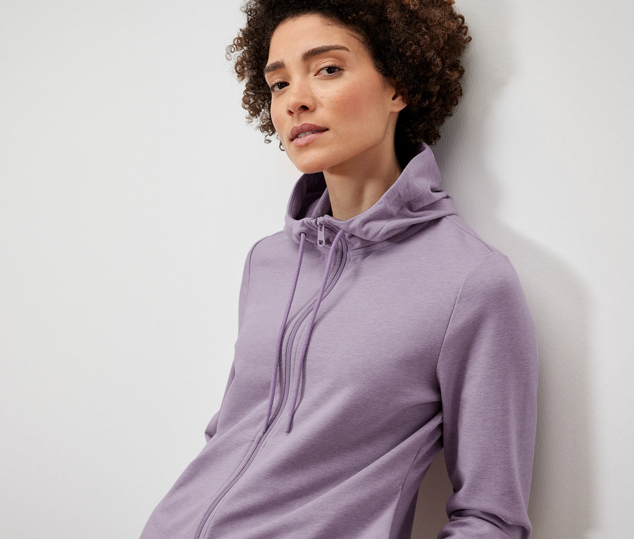 Žena pózuje v lila mikině.