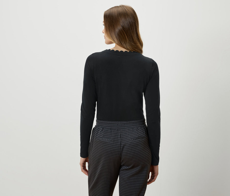 Zezadu pohled na ženu s hnědými vlasy v černém topu s dlouhým rukávem a šedočerných kalhotách.