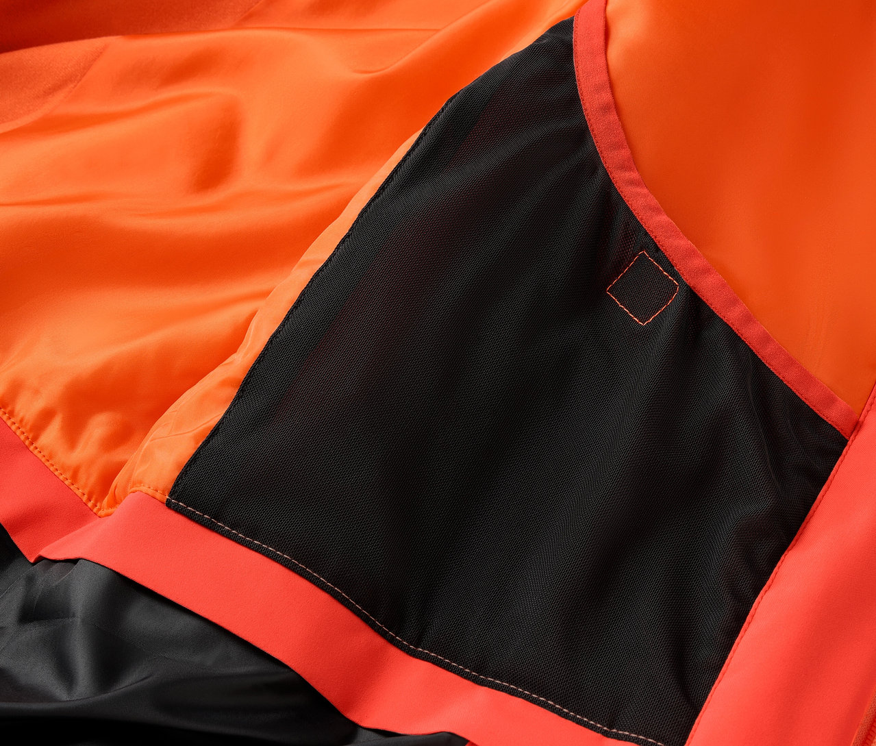 Detail oranžové bundy s černou kapsou.