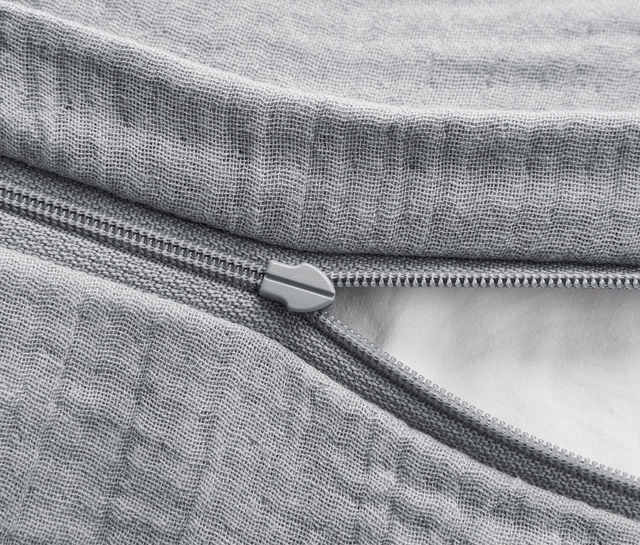 Detail šedého povlečení se zipem, který je částečně rozepnutý a odhaluje bílou výplň.