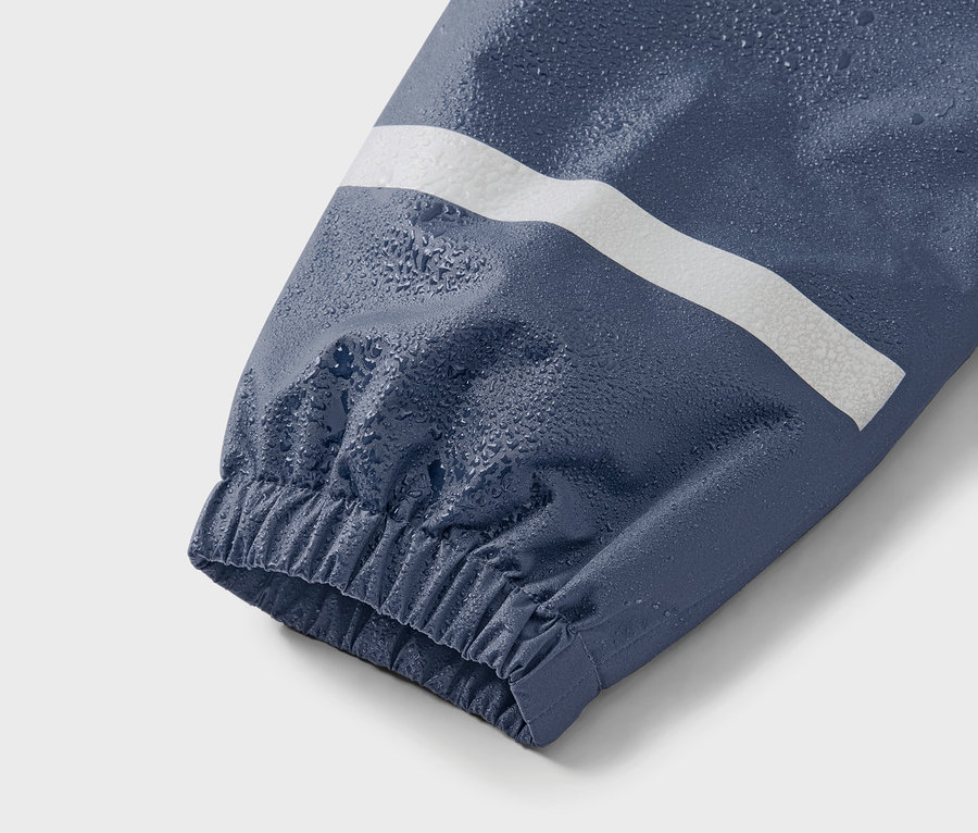 Detailní záběr na modrý rukáv bundy s bílým pruhem a kapkami vody.