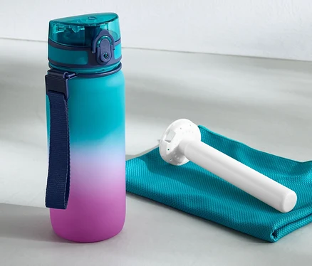 Lahvička na pití s chladicí vložkou stojí vedle ručníku a kettlebell činky.