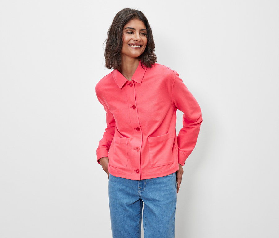 Žena pózuje v růžové žerzejové bundě.