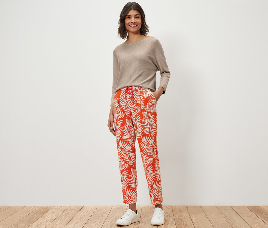 Žena stojí a má na sobě béžový top a žerzejové kalhoty s potiskem.