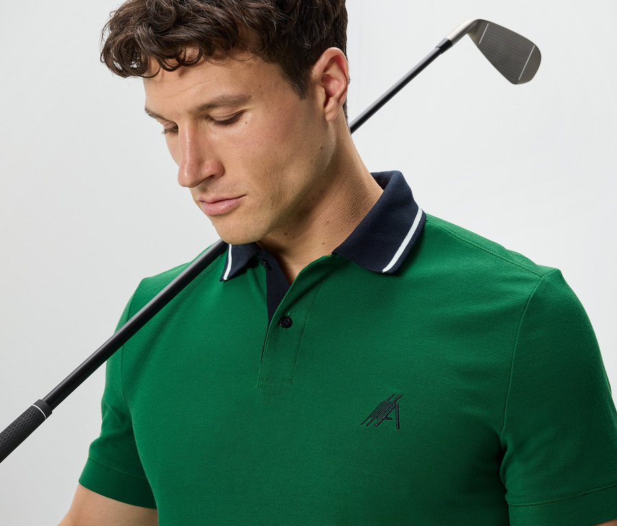Muž s golfovou holí přes rameno má na sobě zelenou polokošili.