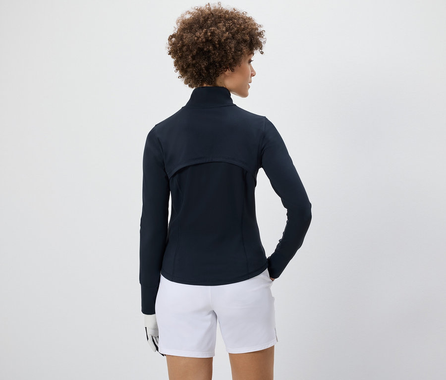 Žena má na sobě funkční bundu a bílé šortky.