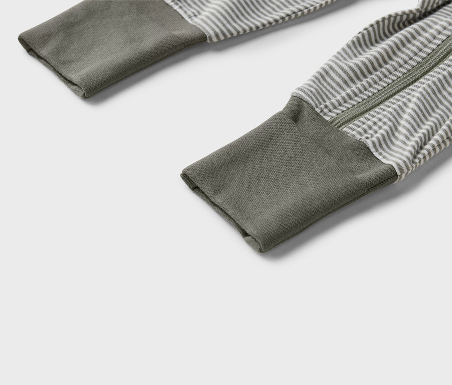 Rukávy šedého a bílého pruhovaného pyžama s celopropínacím zipem a olivově zelenými manžetami.