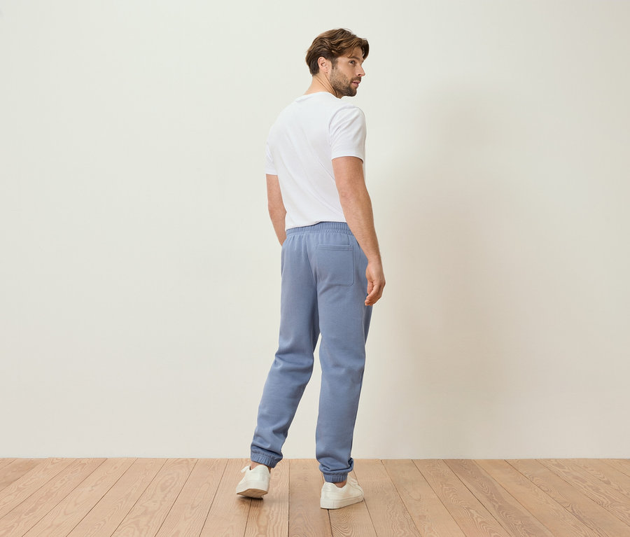 Muž ve světle modrých teplácích a bílém tričku, pohled zezadu.