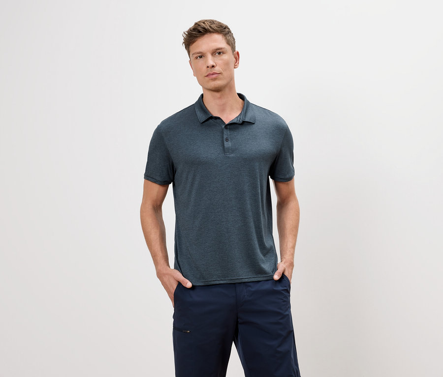 Muž v modrém polo tričku a modrých šortkách stojí na bílém pozadí.