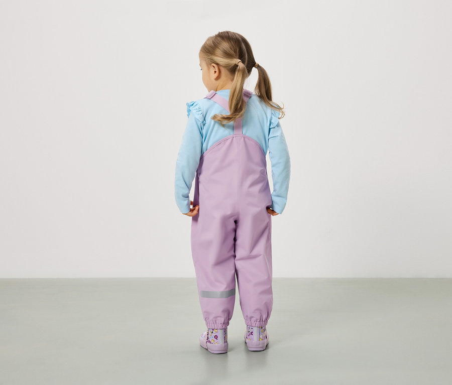 Dívka s culíky stojí zády ke kameře a má na sobě fialové kalhoty a boty.