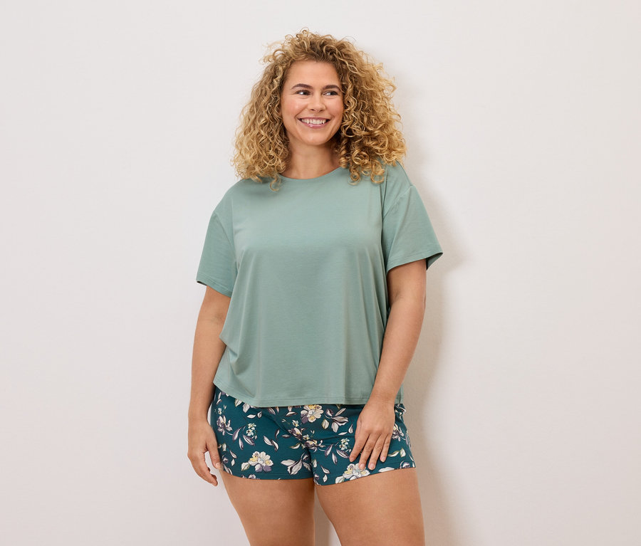 Žena s kudrnatými vlasy v zeleném tričku a květinových šortkách.