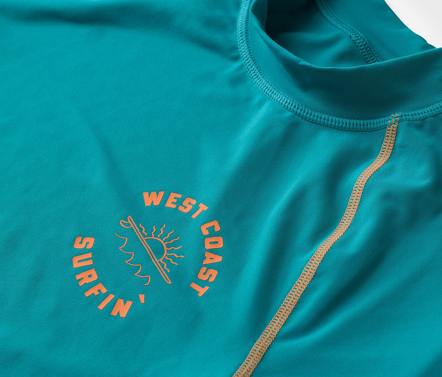 Detailní záběr na tyrkysové tričko s dlouhým rukávem s oranžovým logem "West Coast Surfin".