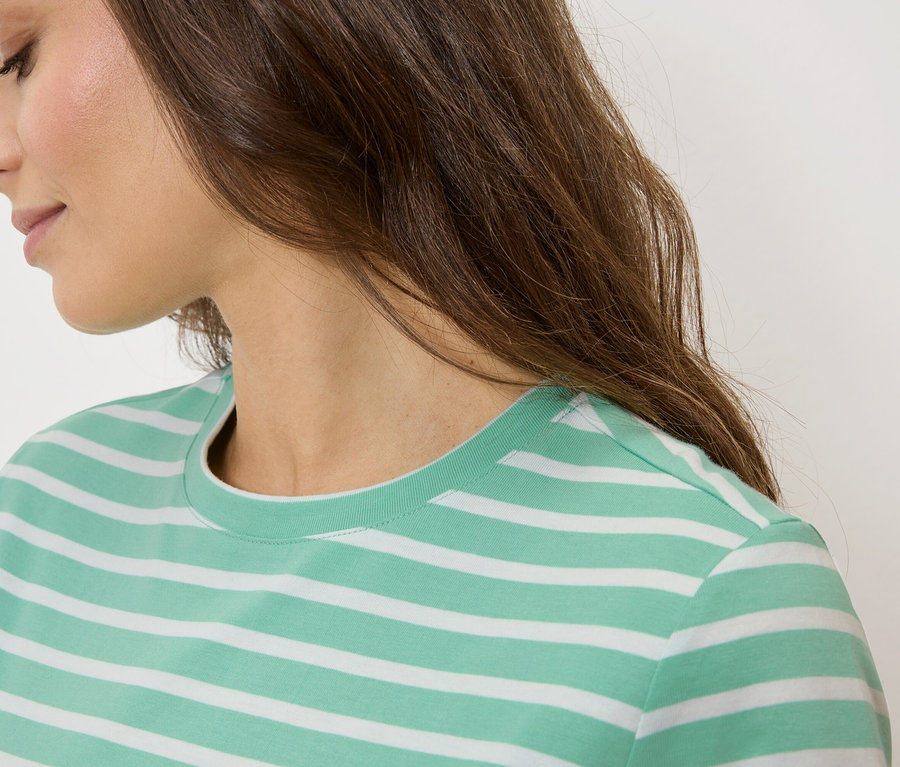 Detailní záběr ženy s hnědými vlasy v zeleno-bílém pruhovaném tričku.