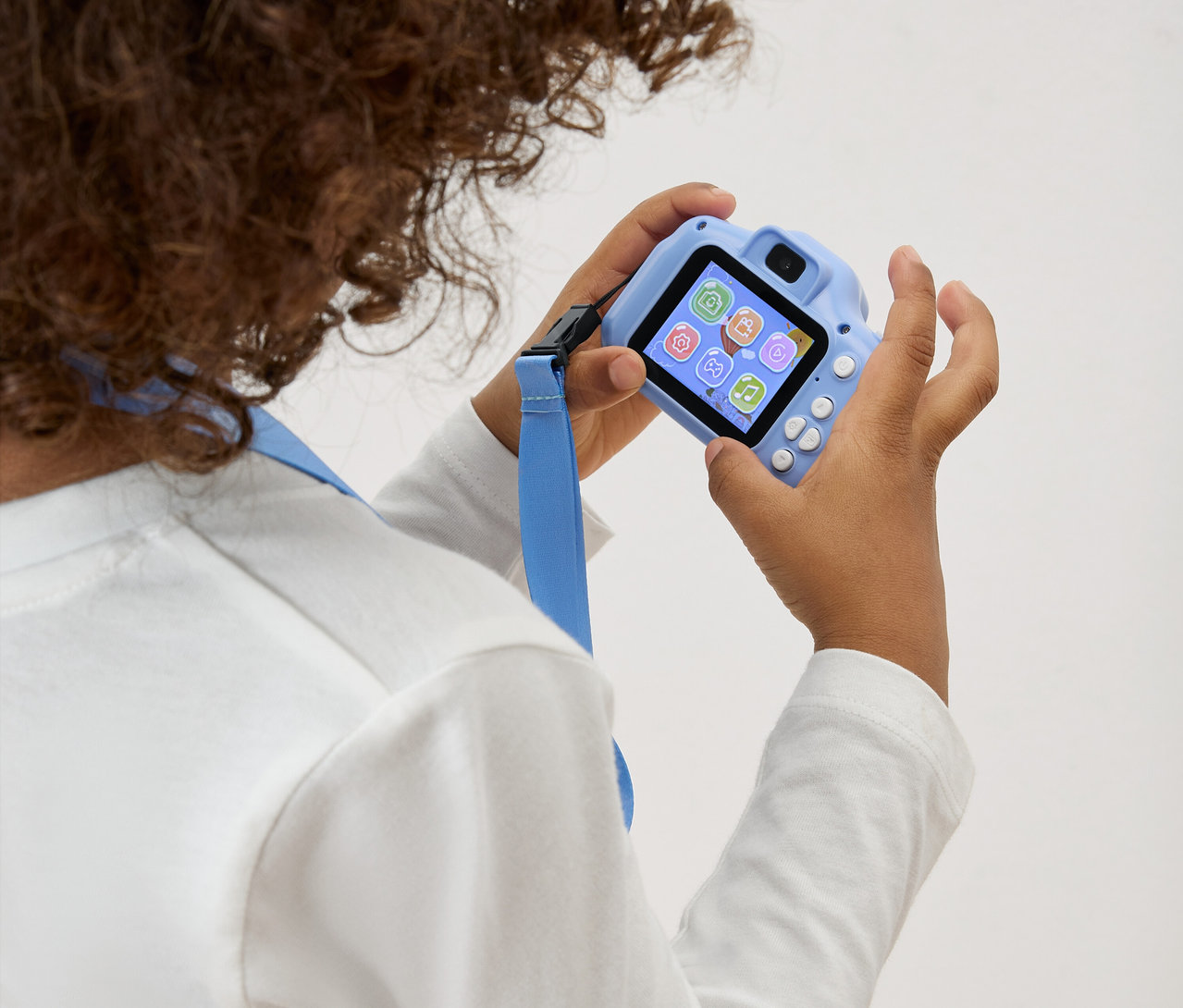 Dítě drží před sebou světle modrý hračkový fotoaparát s modrým popruhem.