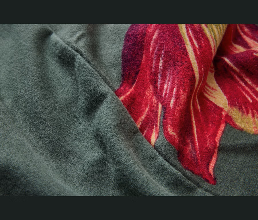 Měkká, tmavě zelená látka, složená tak, aby odhalila velký červeno-žlutý květinový vzor na zeleném pozadí.