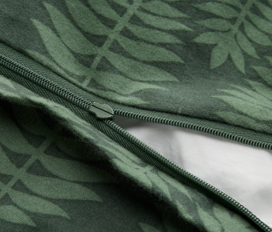 Detail tmavě zelené látky se světle zeleným listovým vzorem. Zelený zip je částečně rozepnutý a odhaluje bílou látku pod ním.