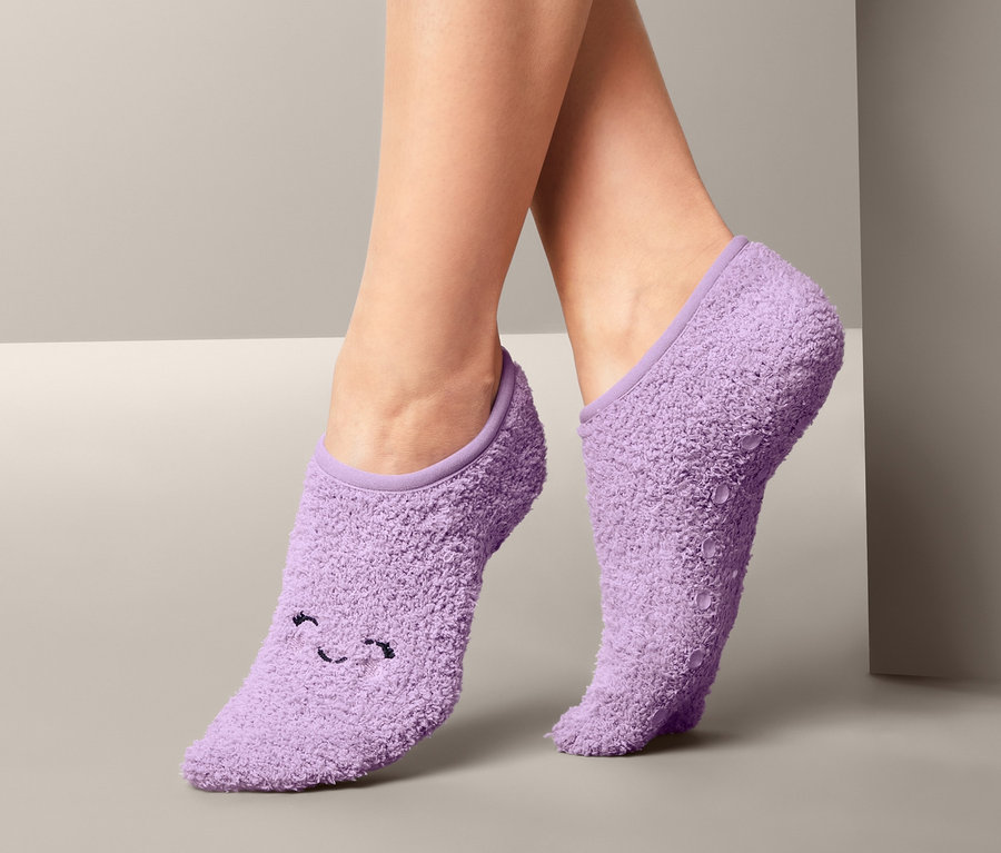 Nohy ženy v páru fialových ponožkových papučí s obličejem.