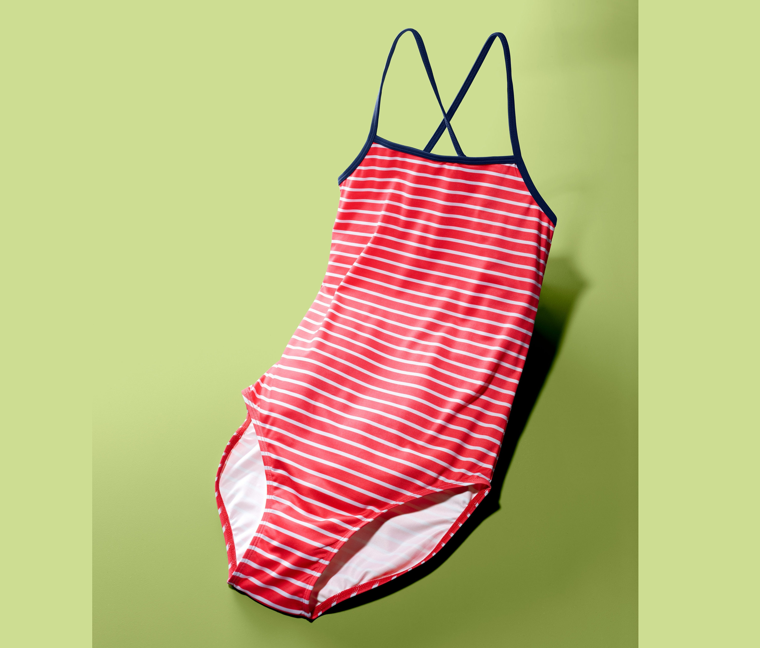 Červeno-bílý pruhovaný jednodílné plavky s tmavě modrými ramínky na zeleném pozadí.