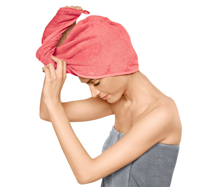 Žena si upravuje růžový ručníkový turban na hlavě, tělo má omotané šedým ručníkem.