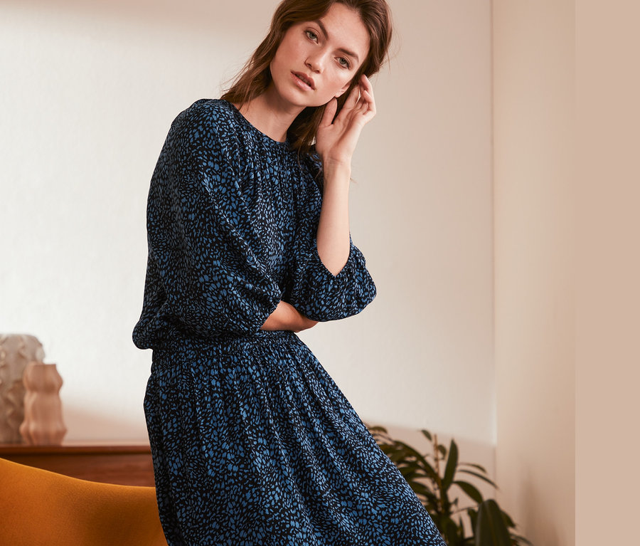 Žena pózuje v modrých šatech s potiskem halenky.