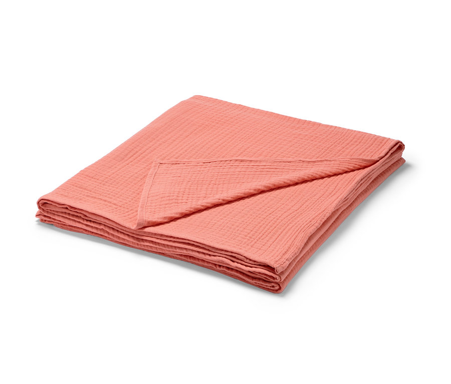 Složený broskvový přehoz na postel z mušelínu.